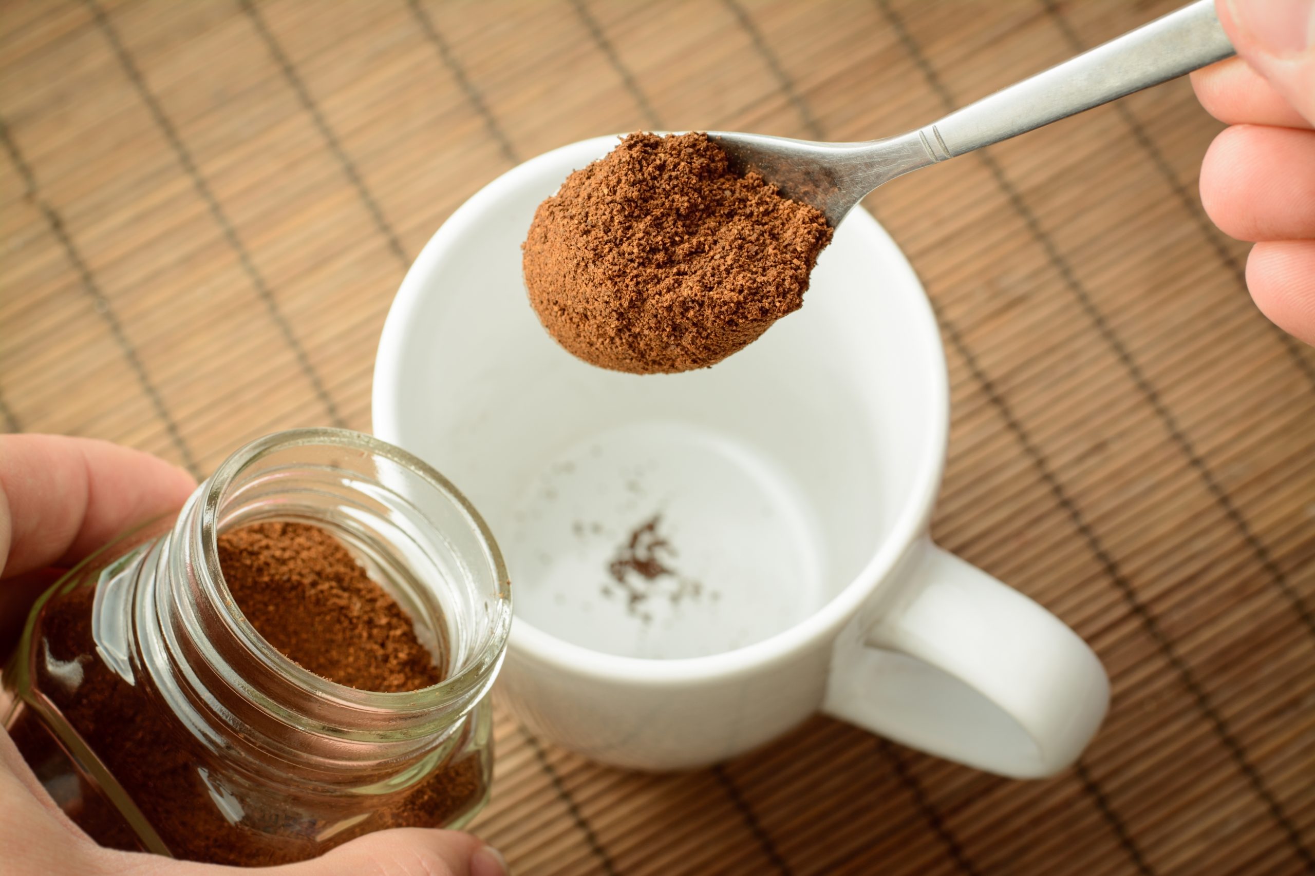 Hand pours instant coffee into a mug.